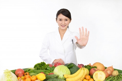 野菜や果物を前にした白衣の女性が手でストップをかけている様子
