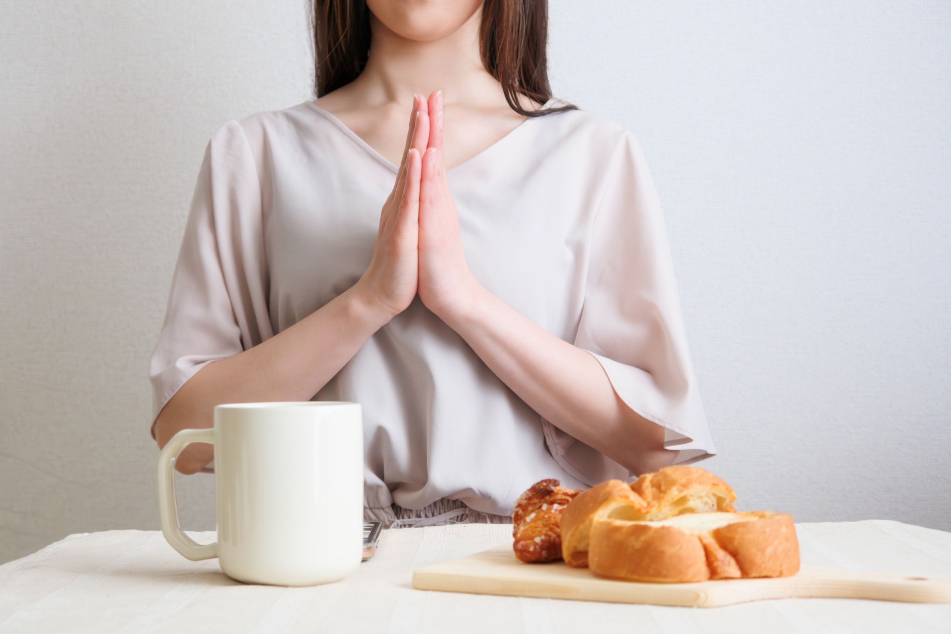 パンとコーヒーの朝食を前に、いただきますのポーズをする女性